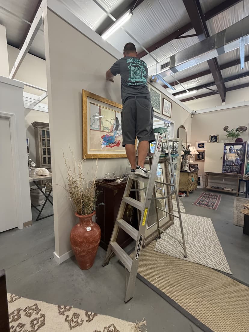 Beach House Moving crew member on a ladder hanging framed artwork during a white-glove move in Santa Rosa Beach, FL