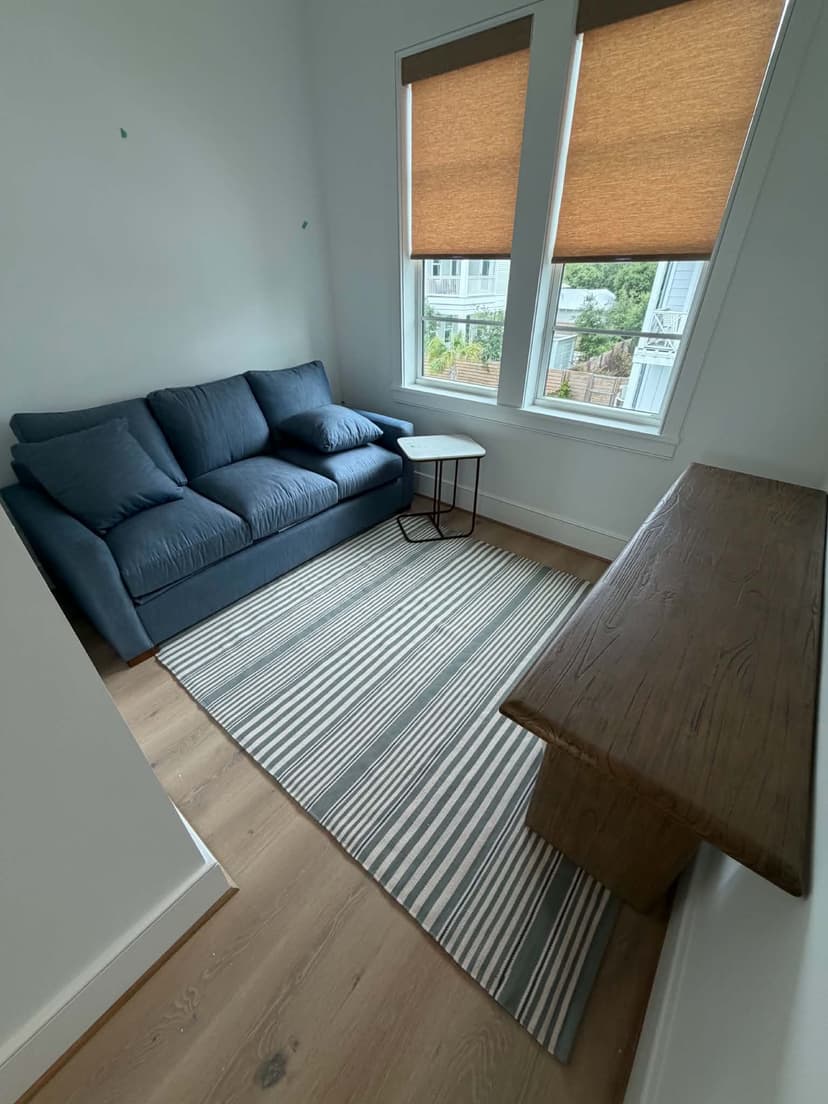 A new-construction den staged by Beach House Moving with a blue sofa, striped rug, and live-edge bench on 30A