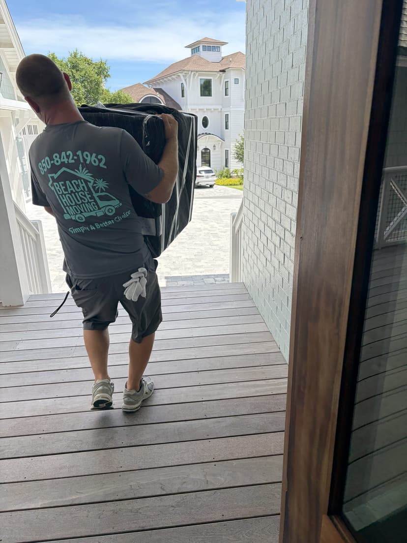 Beach House Moving owner carrying a padded, shrink-wrapped piece into a luxury beach home in Santa Rosa Beach, FL