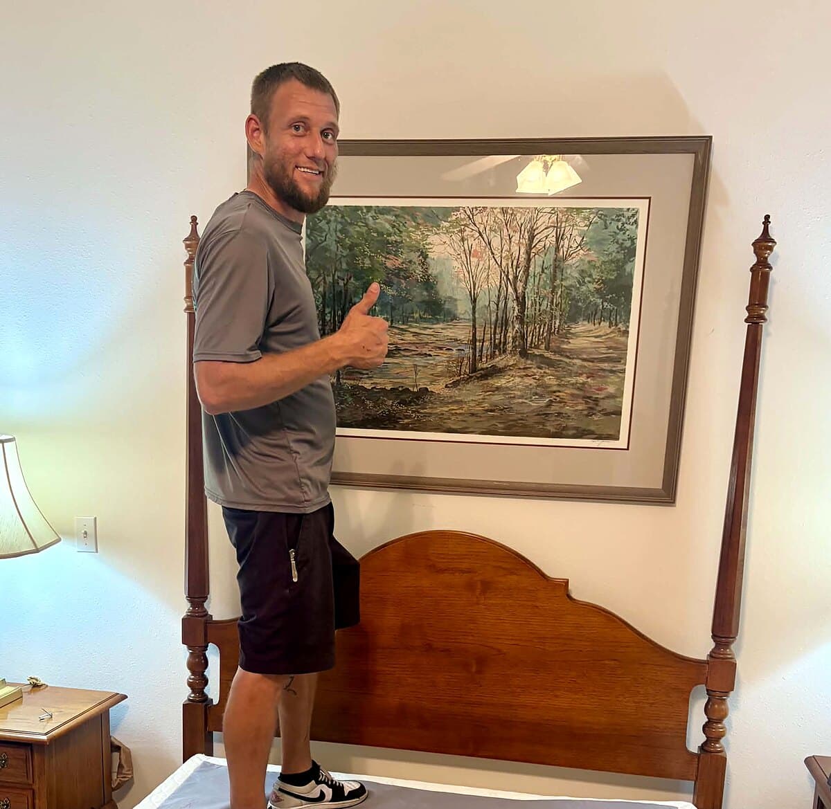 Beach House Moving owner Les hanging a framed landscape above a four-poster bed at a Lily Pads Interiors estate sale in Niceville, FL